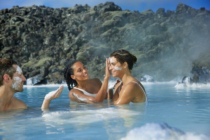 People enjoying a soak in a geothermal hot spring with mist rising and rocky terrain in the background.